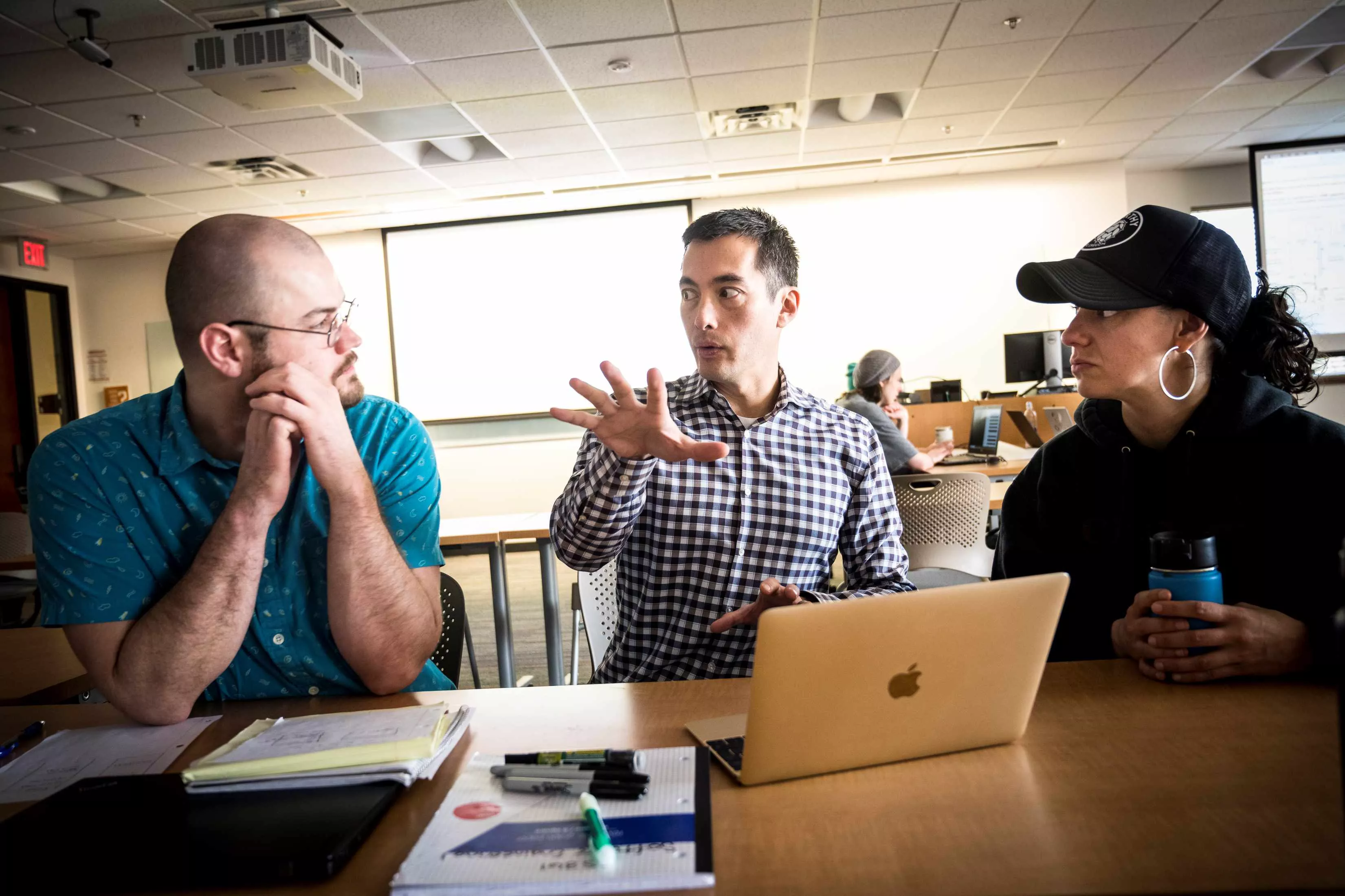 Two students sitting at a table with their instructor who is explaining a concept. 